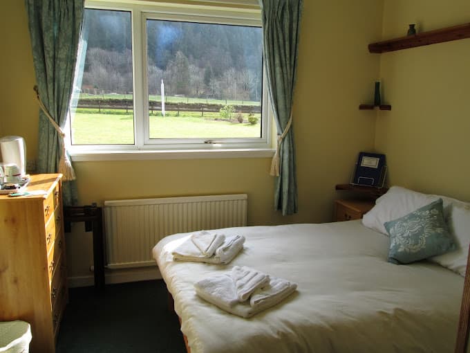 Bedroom with made bed and window view of grassy field and wooded hill
