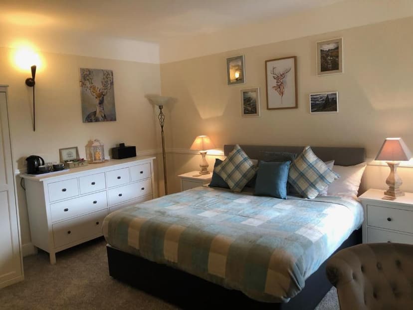 Bedroom with plaid bedding, deer artwork, and white dresser, likely in Glenmoriston Arms Hotel.