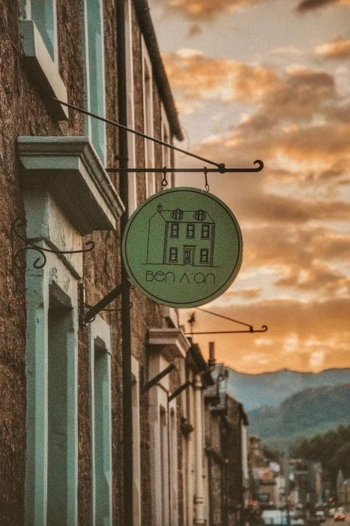 Ben A'an House Inn sign hanging on stone building against sunset sky and mountains.