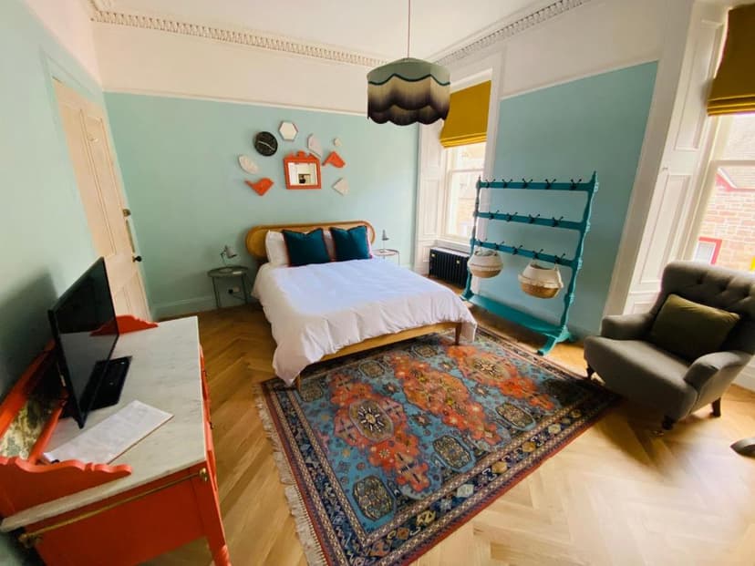 Bedroom in Ben A'an House with light blue walls, wood floor, and colorful rug.