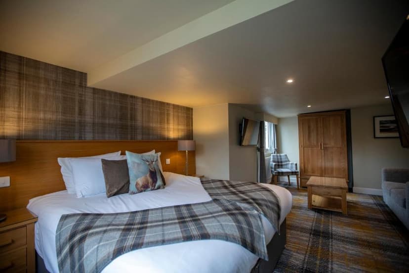 Hotel bedroom with plaid accents, stag pillow, wood furniture, and tartan carpet