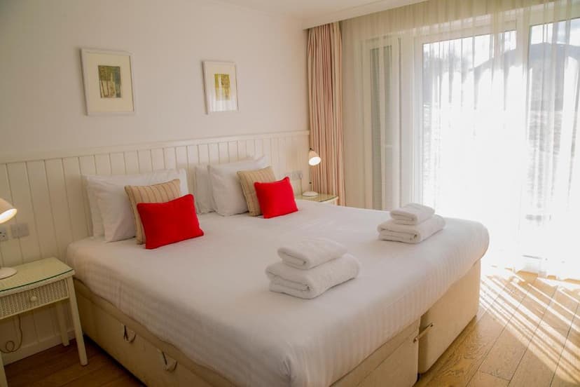 Bright hotel bedroom with white linens, red pillows, and sunlit balcony doors at Bridge of Orchy Hotel.
