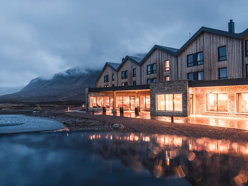 Kingshouse Hotel illuminated at dusk with mountain backdrop reflected in foreground water.