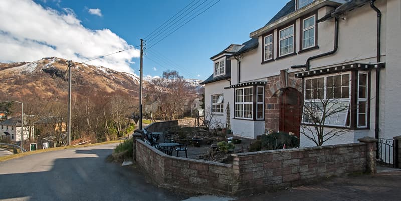 White Bed & Breakfast building with outdoor seating near brown, snow-dusted mountain.