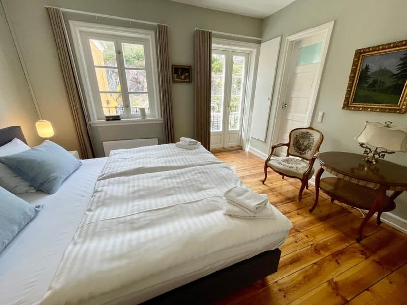 Hotel room with white striped bedding, wooden floors, and windows showing an outdoor view.