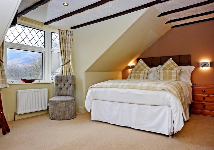 Attic hotel bedroom with plaid bedding, bay window view of hills, and exposed beams