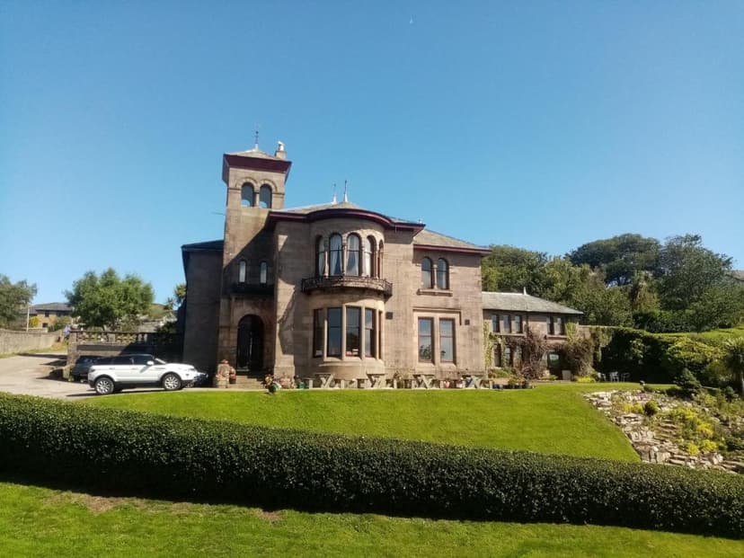 Stone hotel building with tower, manicured lawn, and parked SUV under clear blue sky.
