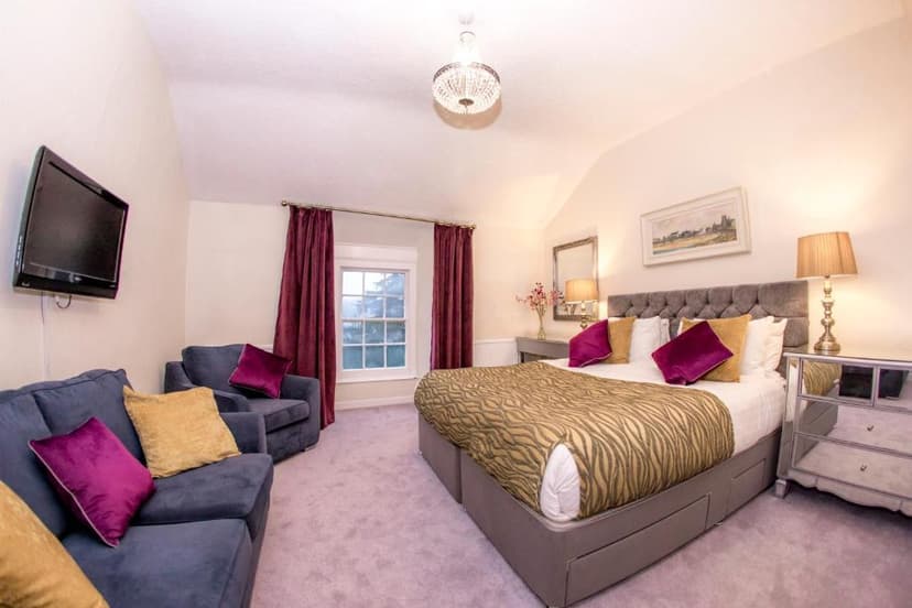 Hotel bedroom with large bed, blue sofa, wall-mounted TV, and window with purple curtains.