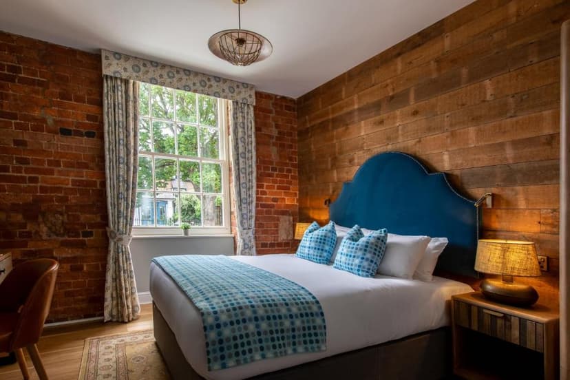 Bedroom with blue headboard, exposed brick, wood paneling, and window view of greenery.