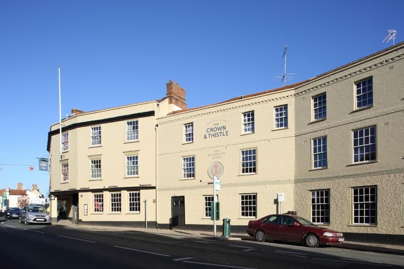 The Crown & Thistle pub building on a street with parked cars under a clear blue sky.