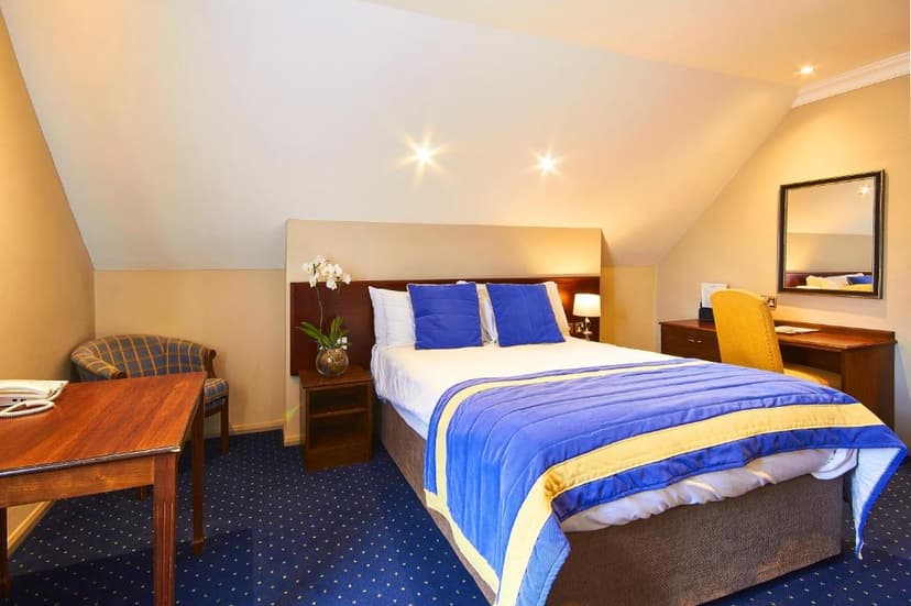 Bedroom in The George Hotel with sloped ceiling, blue and yellow bedding, and dark blue carpet.