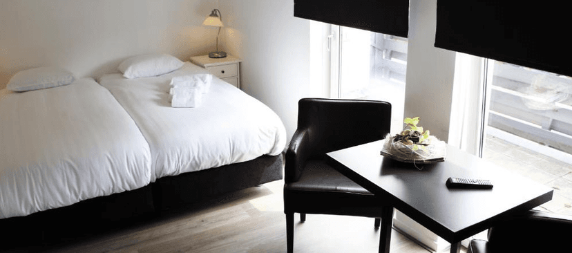Twin beds with white linens, black table, leather chair, and bright window in a modern room.