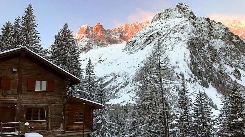 Wooden Auberge de Maya Joie cabin in snowy alpine setting with sunlit peaks