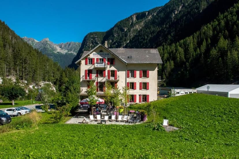 Auberge Mont-Blanc hotel with red shutters nestled in a green valley with steep, forested mountains.
