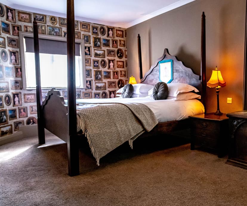 Four-poster hotel bed in room with walls covered in many framed antique portraits