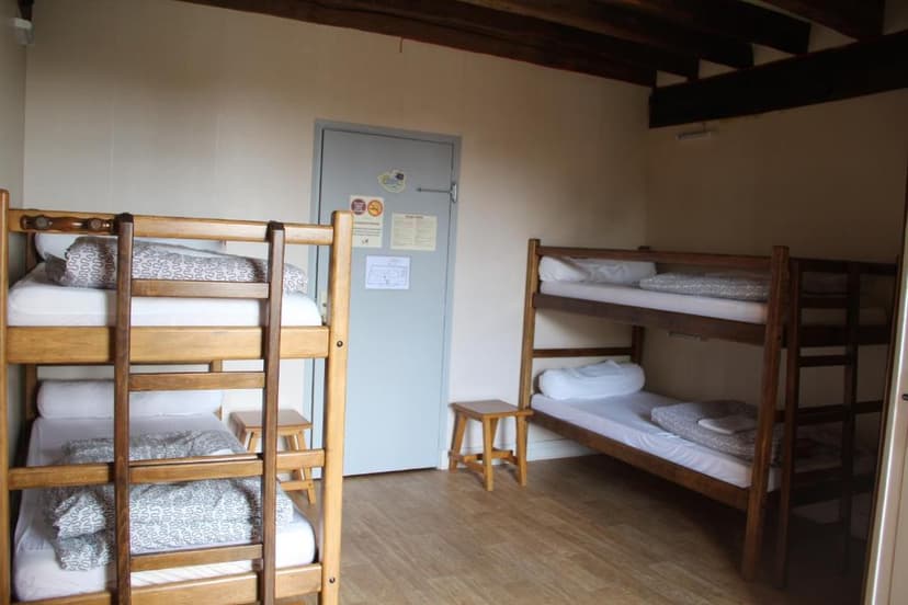 Two wooden bunk beds with white and patterned bedding inside a room with light walls and wooden beams.