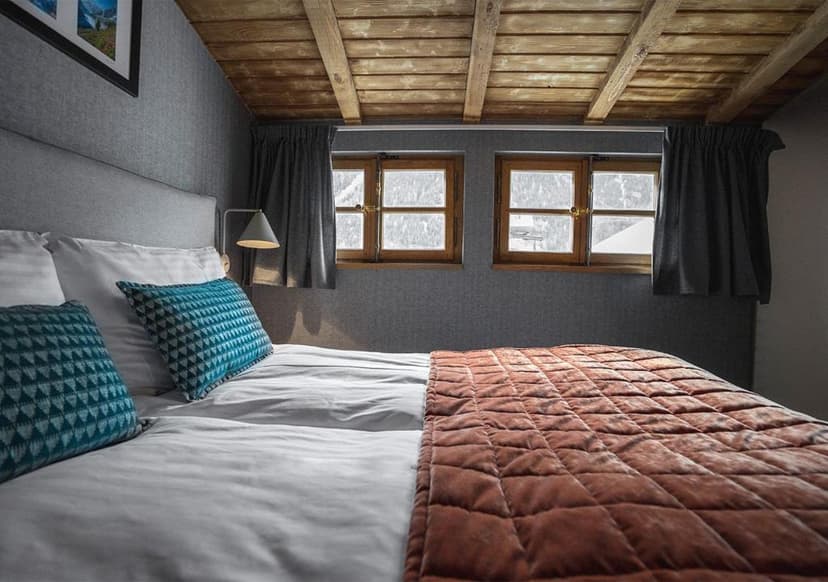 Cozy hotel bedroom with wooden ceiling, gray walls, and view of snow outside windows.