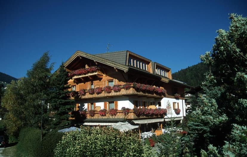 Wooden alpine hotel with flower boxes on balconies against a clear blue sky and forested mountain.
