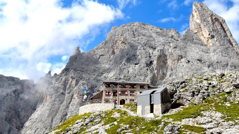 Rifugio Pradidali mountain hut nestled against massive grey rock peaks under a blue sky.