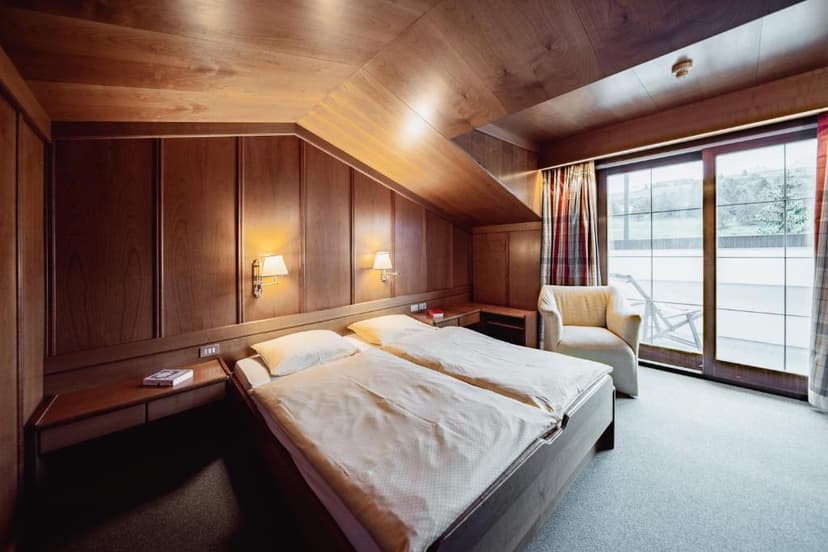 Hotel room with wood paneling, twin beds, and balcony access overlooking green landscape.