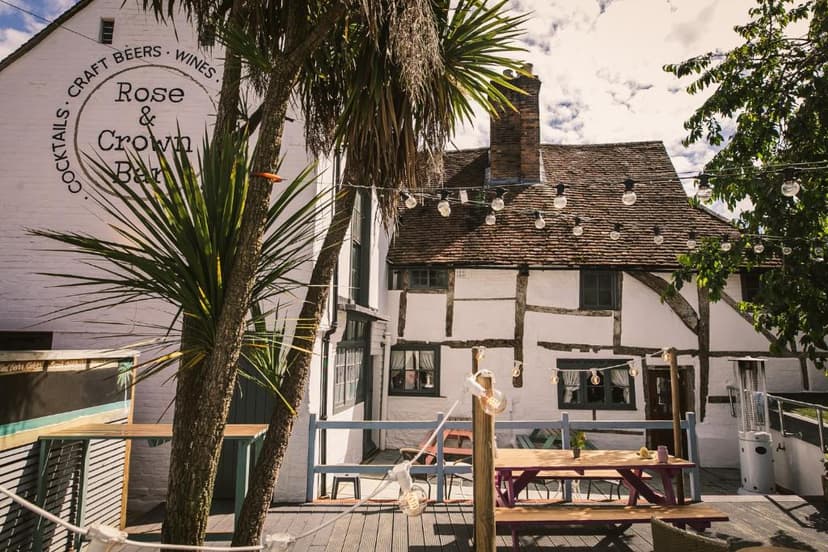 Rose & Crown Bar patio with palm trees, string lights, and timber-framed building.