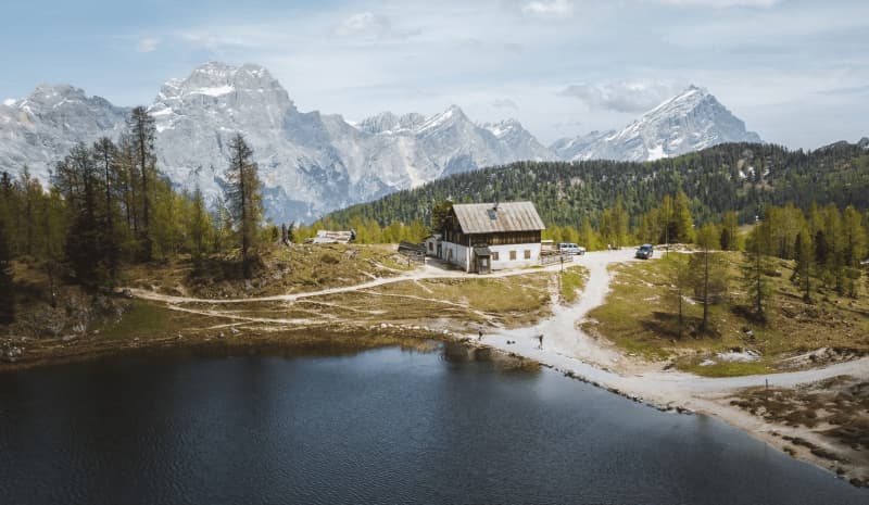 Rifugio Croda da Lago hut by dark alpine lake with snowy mountains in background