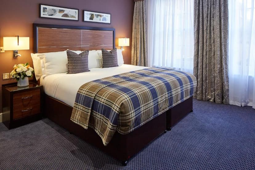 Bedroom with large bed, blue plaid throw, and window with sheer curtains at Sir Christopher Wren Hotel.
