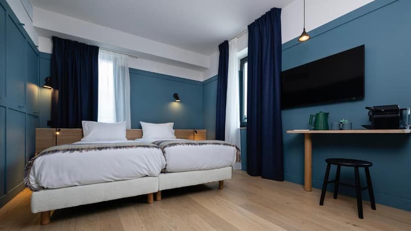 Twin beds in modern hotel room with blue walls, wood floor, and wall-mounted TV
