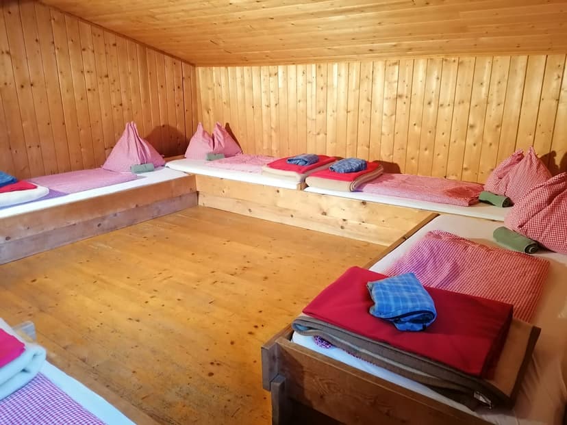 Bunk room with wooden walls and floors, set with simple beds, red gingham pillows, and blankets.