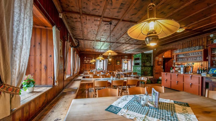 Rustic dining room with wood paneling, tables, chairs, and a green tiled stove, Karwendelhaus.