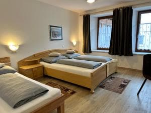 Wooden double bed and single bed in a bright room with light wood floors and dark curtains.