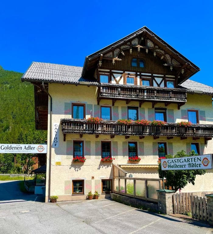 Gasthof Goldener Adler building with wooden balconies and flower boxes against a clear blue sky.