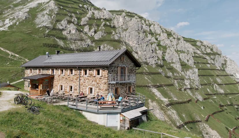 Starkenburger Hütte stone mountain hut with solar panels below steep, terraced green slope.