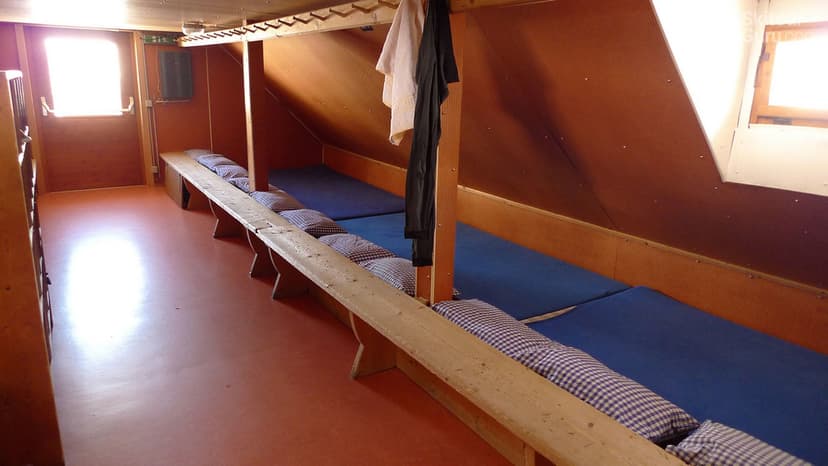 Bunk room interior with wooden benches, blue mattresses, and checkered pillows at Franz Senn Hütte.