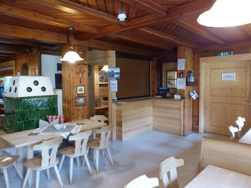 Dining area in Franz-Senn-Hütte with wood paneling and green tiled stove.