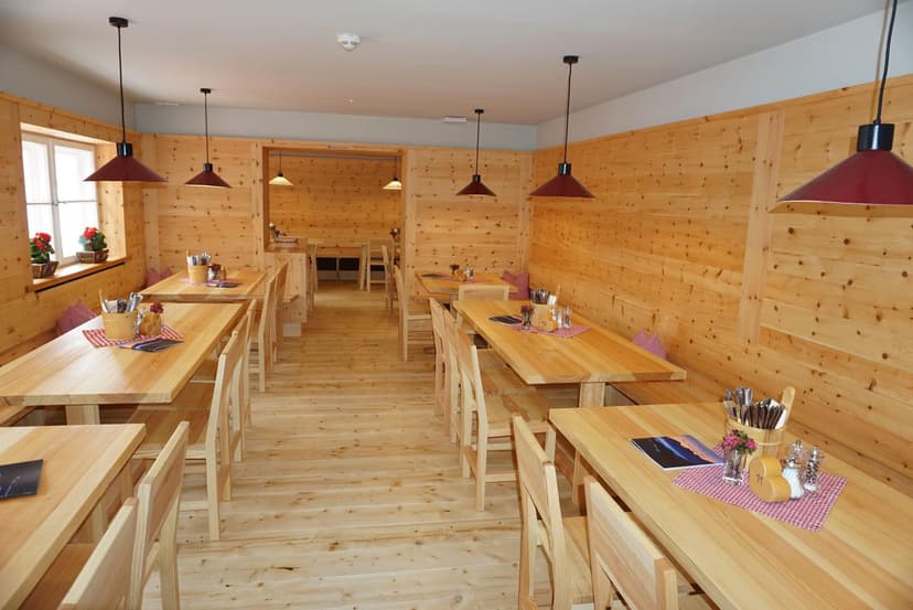 Dining room with light wood paneling, wooden tables, benches, and red pendant lights, likely Neue Regensburger Hütte.