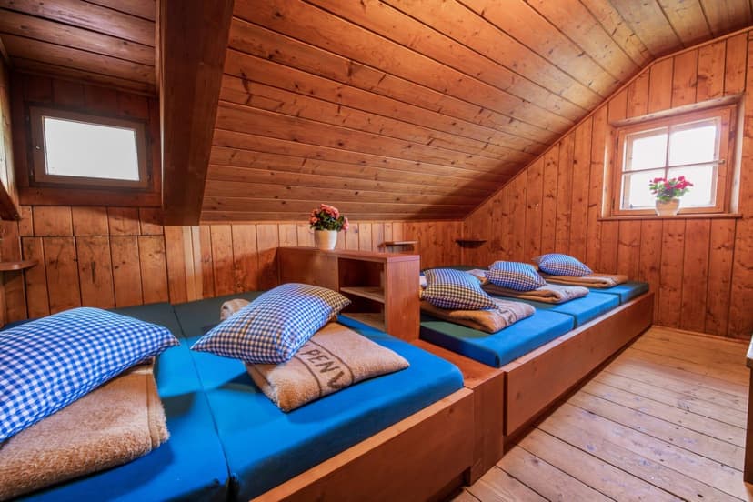 Bunk room with wood paneling, blue mattresses, and gingham pillows at Neue Regensburger Hütte