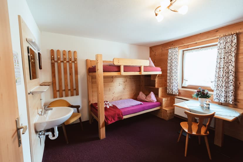 Cozy wooden cabin room with bunk beds, sink, and small dining table.