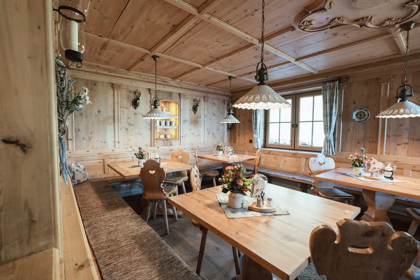 Rustic dining room with light wood paneling, carved chairs, and hanging lamps, likely in an alpine setting.