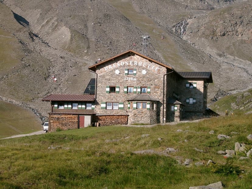 Dresdner Hütte stone mountain refuge with gondolas ascending steep rocky slope in summer.