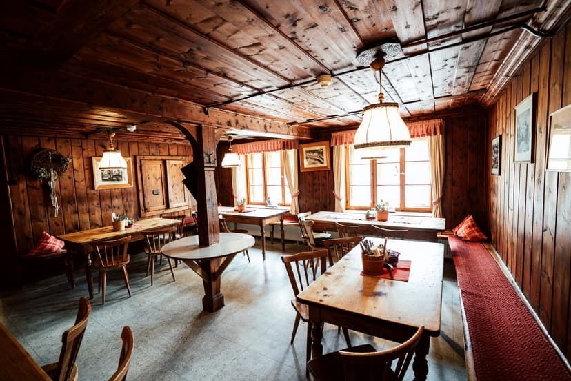Rustic dining room with dark wood paneling, wooden tables, and bright windows at Nürnberger Hütte.