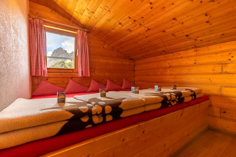 Innsbrucker Hütte bunk room with wood paneling, view of alpine peak through window.