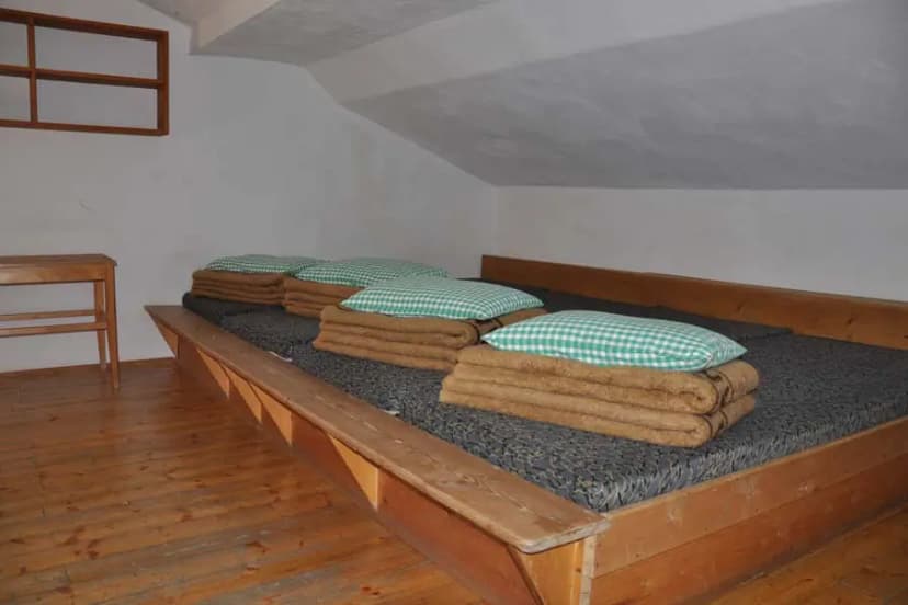 Simple dormitory sleeping area in Schweinfurter Hütte with wooden bunks, blankets, and pillows.