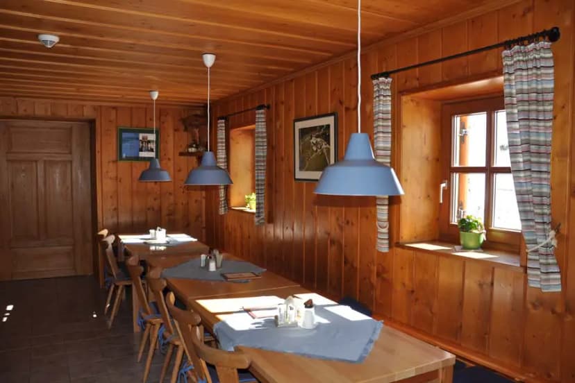 Dining room interior with wood paneling, long wooden tables, and blue pendant lights at Schweinfurter Hütte.