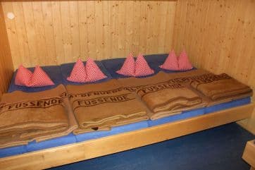 Bunk beds with brown blankets and red-and-white checkered pillows inside a wood-paneled room at Tappenkarseehütte.