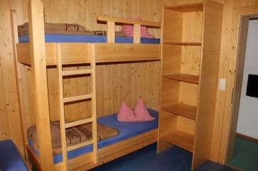 Wooden bunk beds with blue mattresses and red checkered pillows inside a room with wood-paneled walls.
