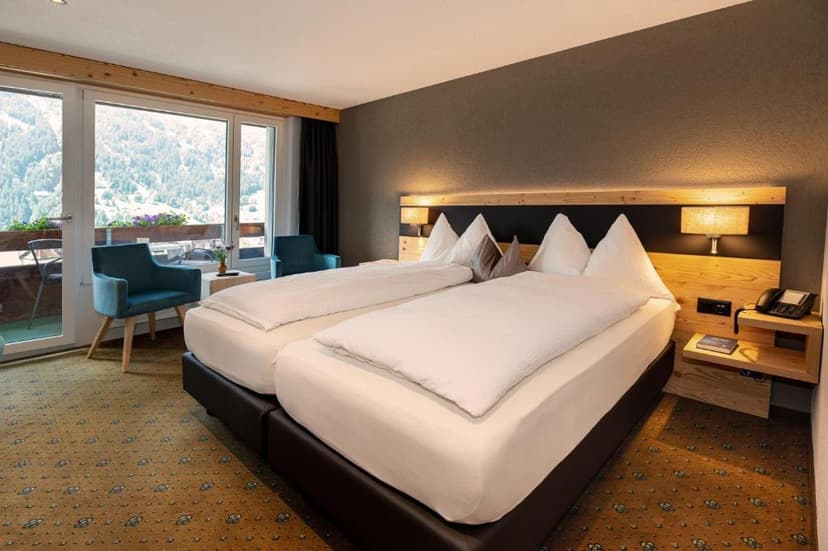 Hotel room with twin beds, balcony access, and view of alpine mountains in Grindelwald.