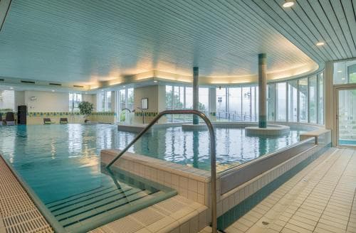 Indoor swimming pool with large windows overlooking a bright outdoor area at Arenas Resort Victoria Lauberhorn.
