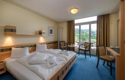 Twin hotel room with wooden furniture, white bedding, and mountain view balcony at Arenas Resort Victoria Lauberhorn.