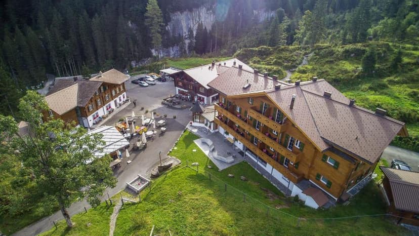 Wooden hotel buildings in Griesalp nestled against a steep, forested mountain slope.